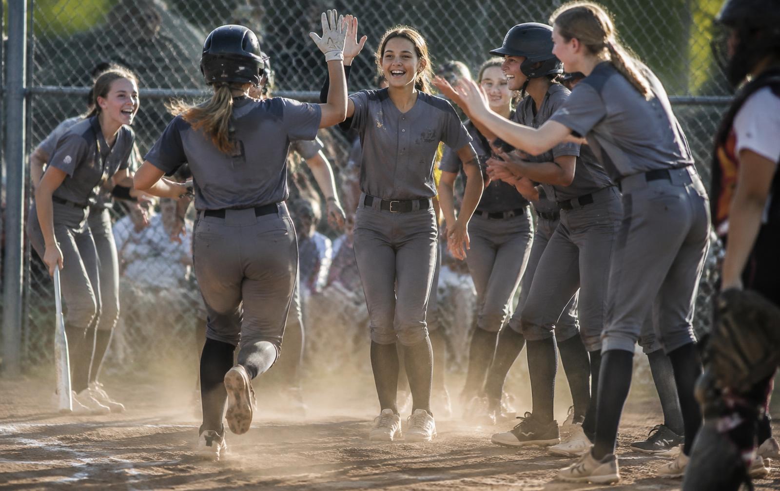 Softball team celebrating a run at home plate